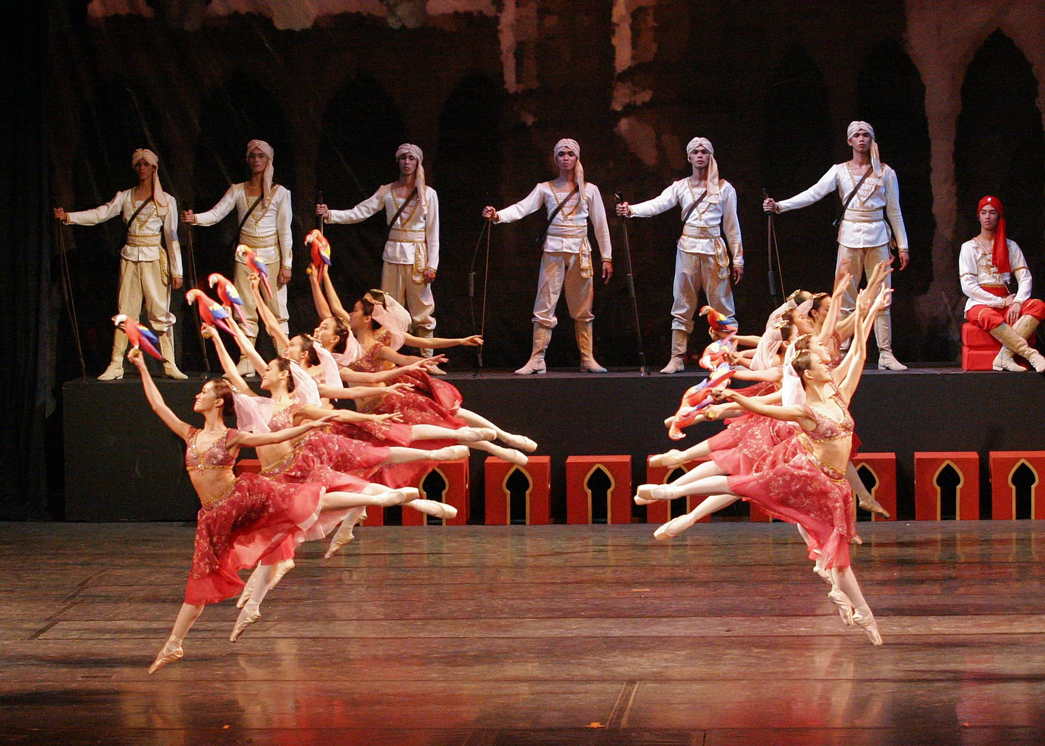    Clad in red dresses accentuated by sparkling beads, the “parrot girls” in  La Bayadere  (2004) engaged in the light-hearted Waltz of the Parrots. The festive colors they wear and the plumed creatures they hold in their hands signify the luxuriousn