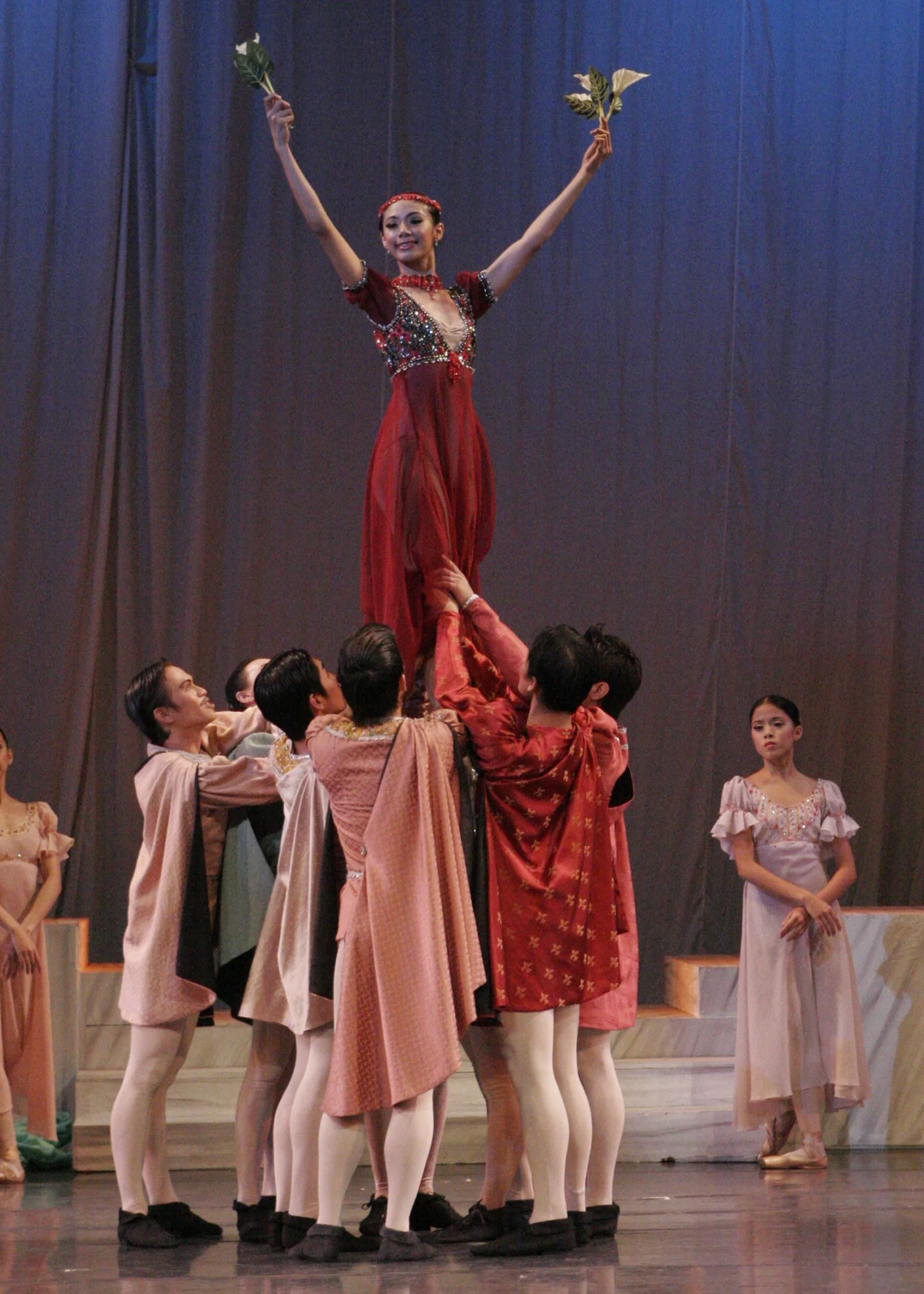    Wearing a maroon dress with sparkly accents and matching accessories on her head and neck, Lady Capulet (Zaira Cosico) is in her element as she is hoisted in the air by young men in  Romeo and Juliet  (2007). Inspired by the Shakesperean work, the