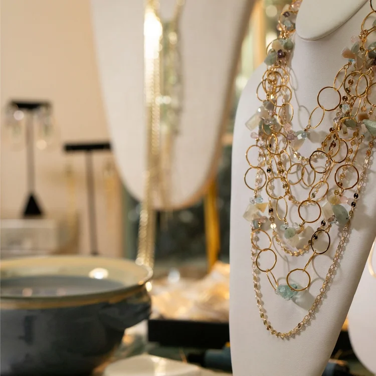 A gold multi-strand necklace of rings and pale gemstones on a display bust in the studio