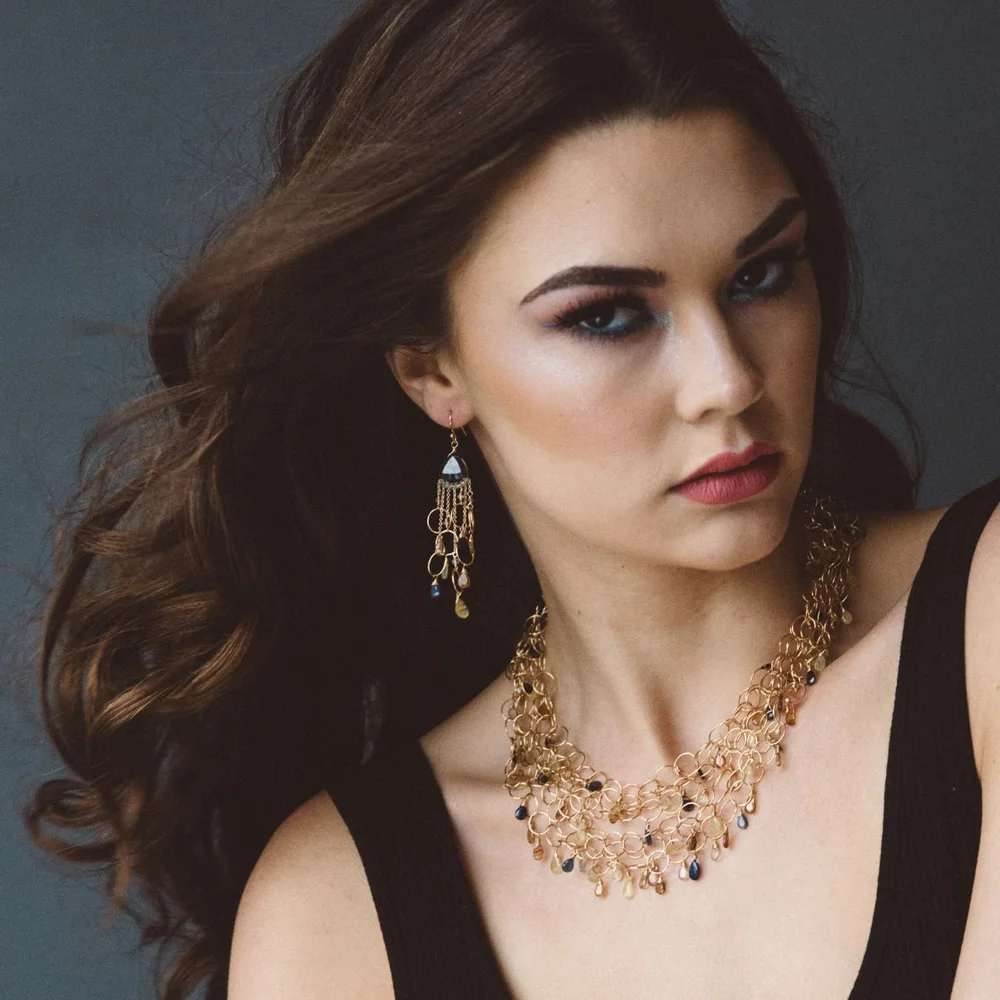 A model wearing long Andrea Li gold fringe chandelier earrings with a gold gemstone bib necklace