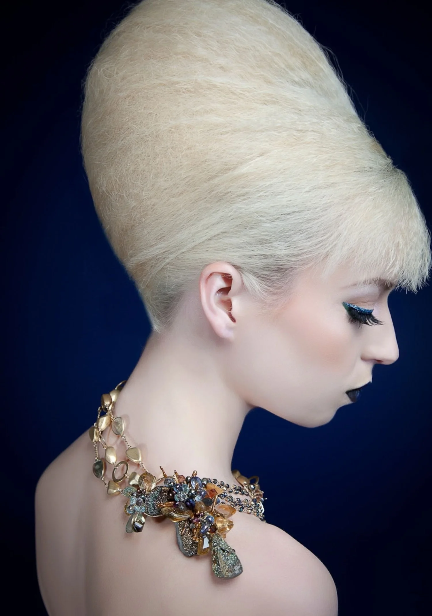 Model with a platinum beehive, seen in profile against deep navy, wearing a rainbow pyrite and gemstone statement necklace by Andrea Li