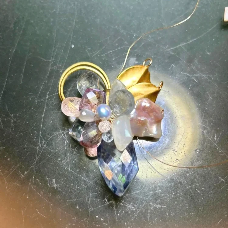 A cluster of pink, lilac and clear gemstones, a pearl and gold leaves wired together on the bench