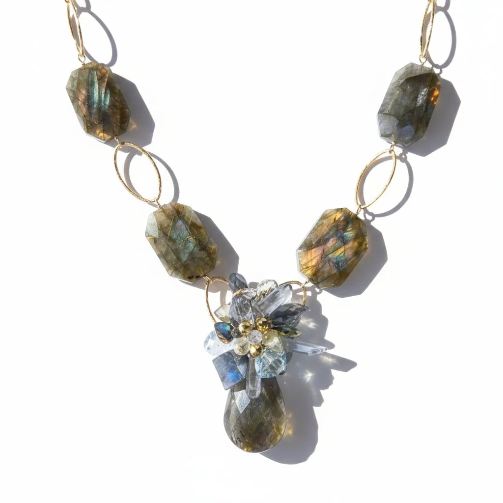 Close-up product photo of a statement necklace with faceted labradorite stones, gold oval links, and a floral-inspired centerpiece accented with blue and clear gemstones, finished with a labradorite teardrop pendant.