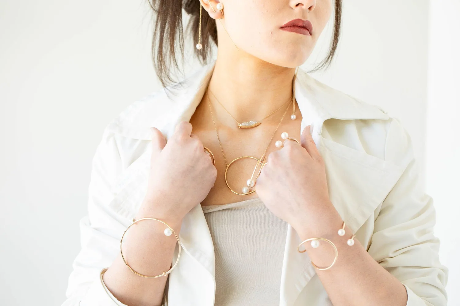 A model in a white shirt wearing Andrea Li gold and pearl bangles on both wrists, by Andrea Li