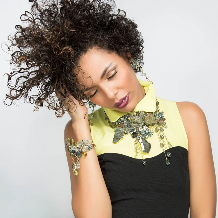 A model with curly hair, eyes closed, wearing a crystal cluster collar and a matching cuff