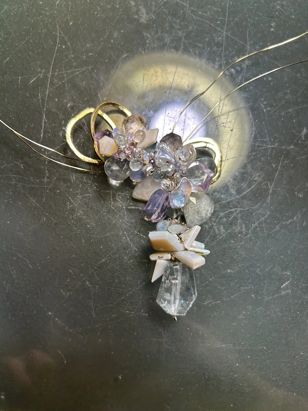 A pastel gemstone cluster mid-build on Andrea Li's bench, its wire ends still loose