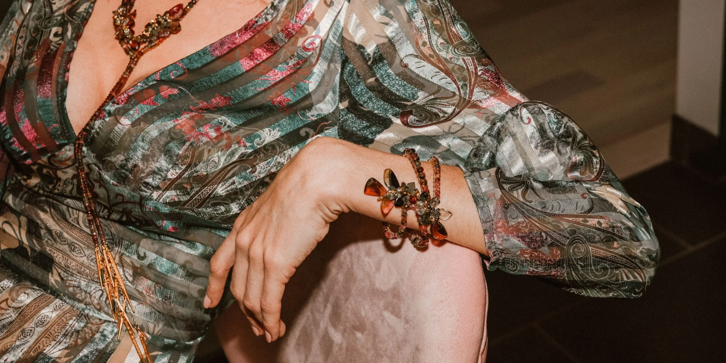 A model in a patterned silk blouse resting her arm, wearing an Andrea Li tourmaline bracelet, by Andrea Li