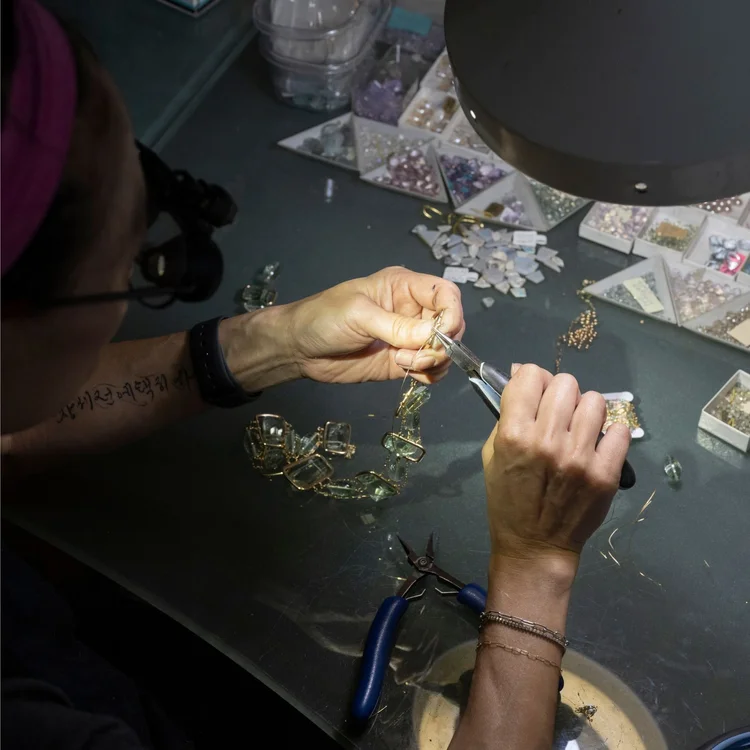 Andrea Li wiring gemstones into a gold necklace over trays of beads