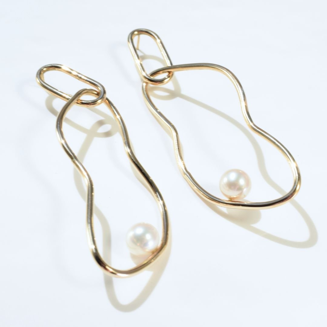 Detailed shot of abstract hoop-shaped statement gold drop earrings, focusing on the lustrous pearl and organic design.