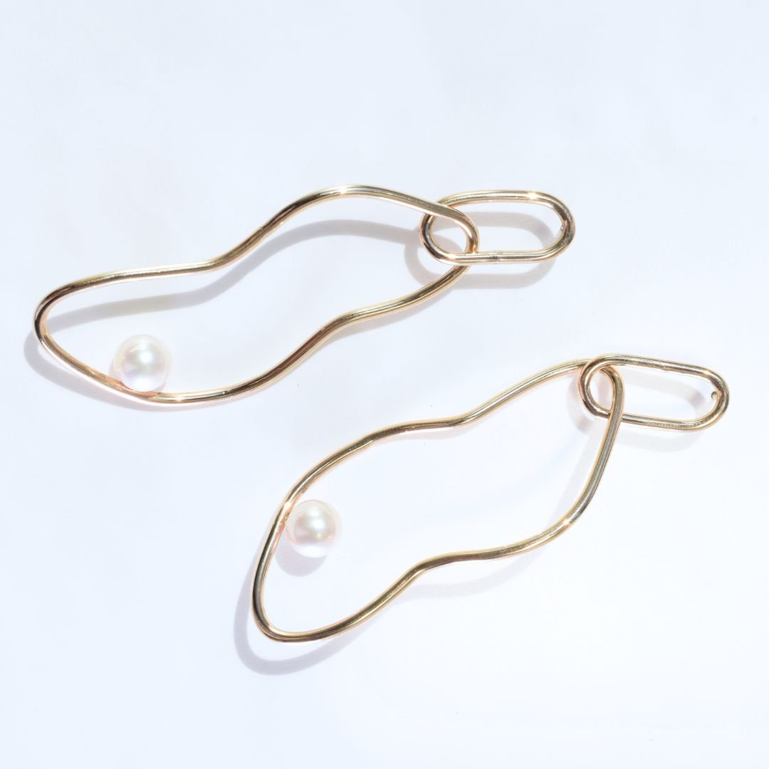 Detailed shot of abstract hoop-shaped statement gold drop earrings, focusing on the lustrous pearl and organic design.