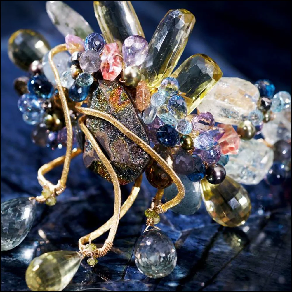 A gold wire statement piece around a dark druzy center with clusters of pastel and clear faceted stones