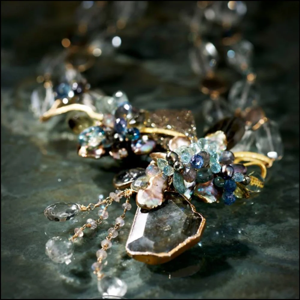 A gold piece with clusters of pale blue and clear faceted stones and dangling drops