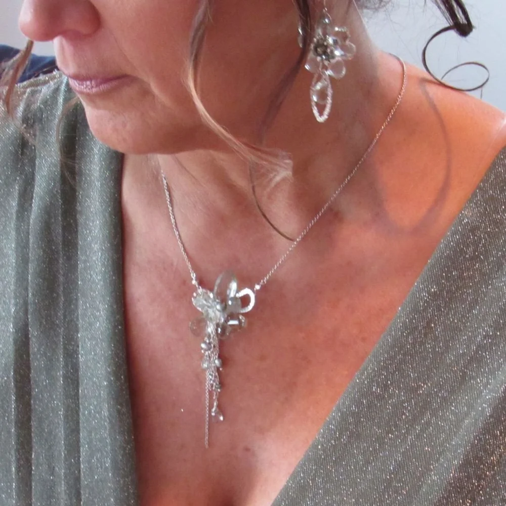 A close view of a woman in a gray-green gown wearing a silver pendant necklace and drop earrings