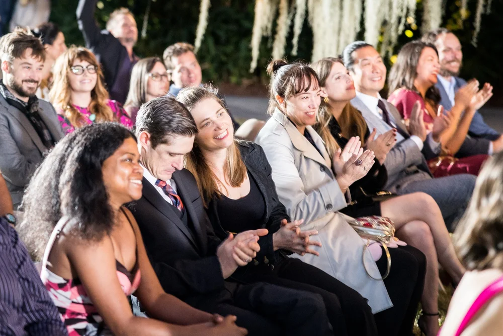 Smiling wedding guests applauding from their seats under string lights