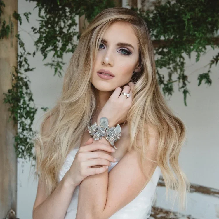 A bride with long blonde hair wearing a crystal cuff and a ring, one hand at her collarbone
