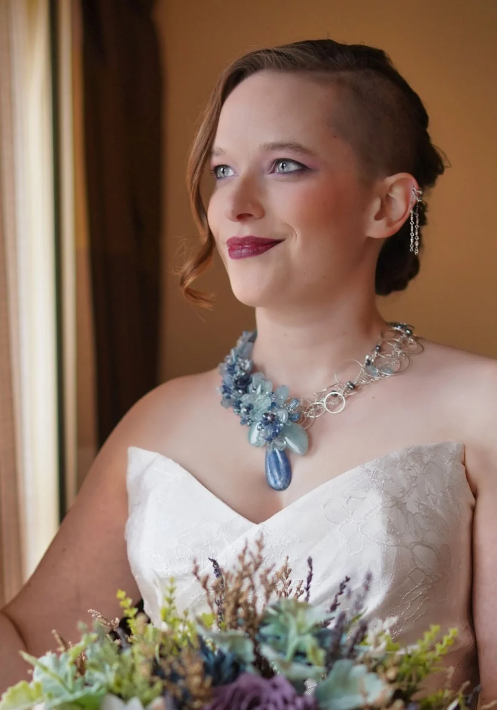 A bride with a side-swept updo wearing a blue gemstone statement necklace
