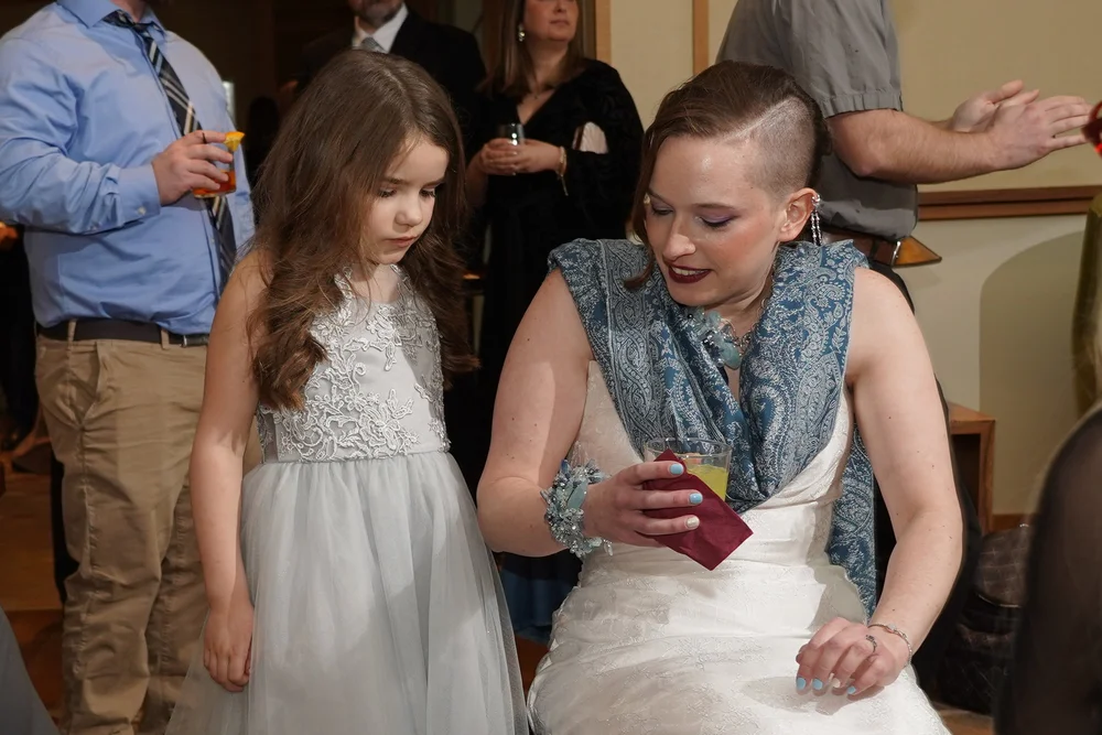 A bride in a blue paisley shawl and a blue cuff sitting beside a young girl in a pale gown at the reception