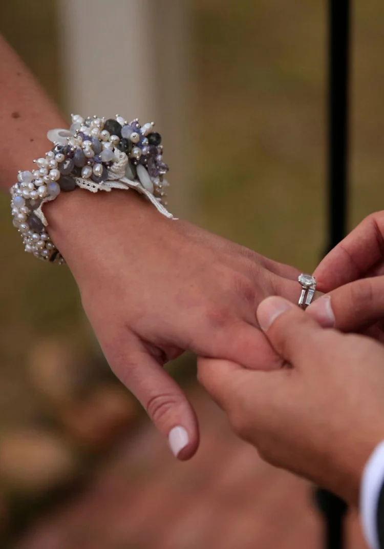 A groom placing a ring on the bride's finger, a silver cluster cuff at her wrist
