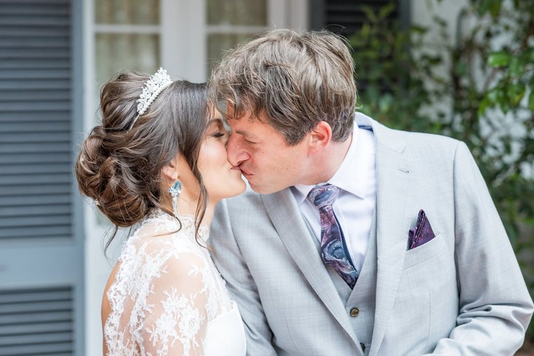 A bride in a tiara kissing the groom in a gray suit