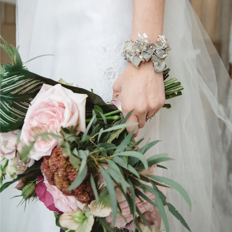 A bride's wrist in a silver cluster cuff, holding a pink and green bouquet