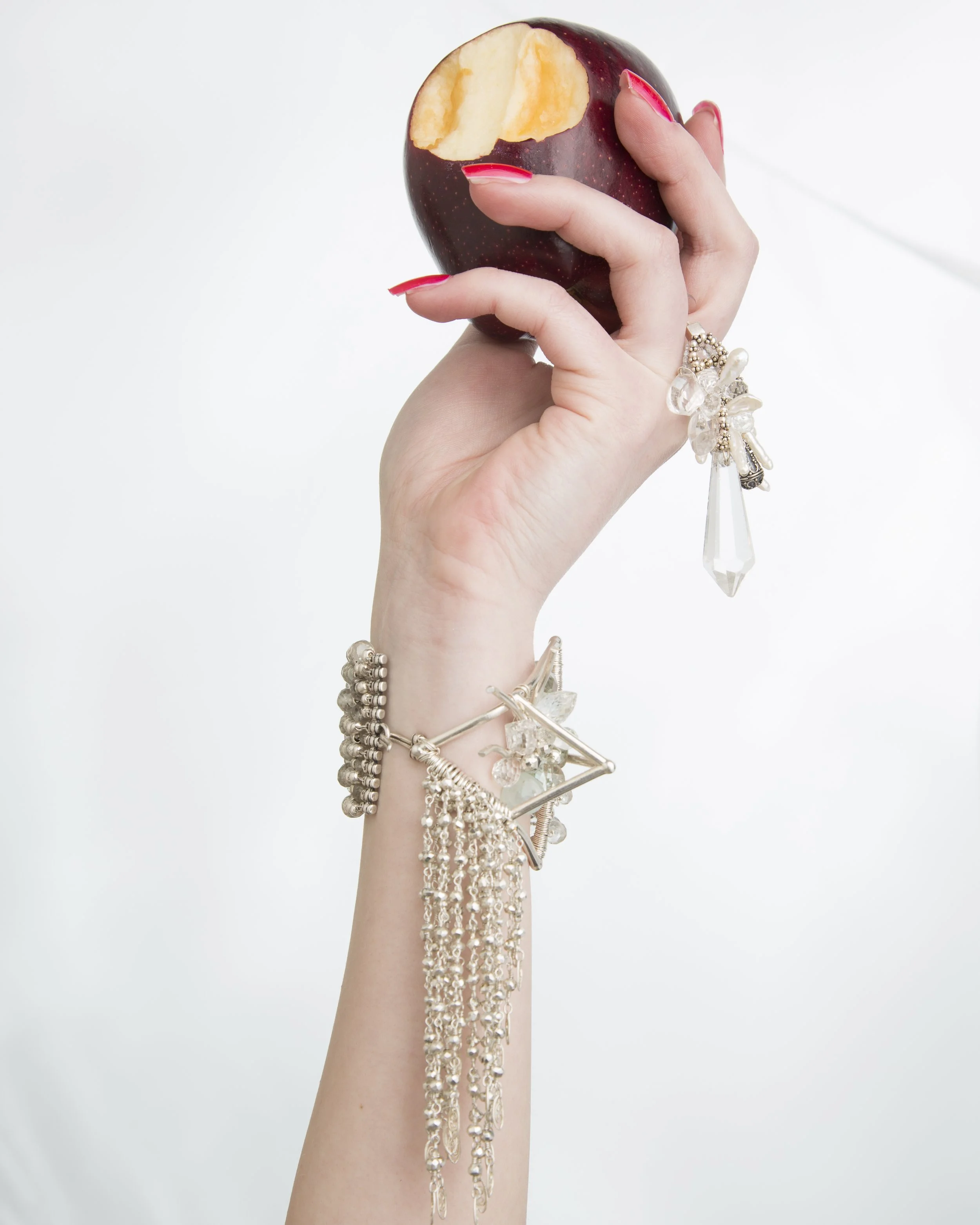 model holding an apple wearing a statement bracelet with silver fringe chains holding a crystal