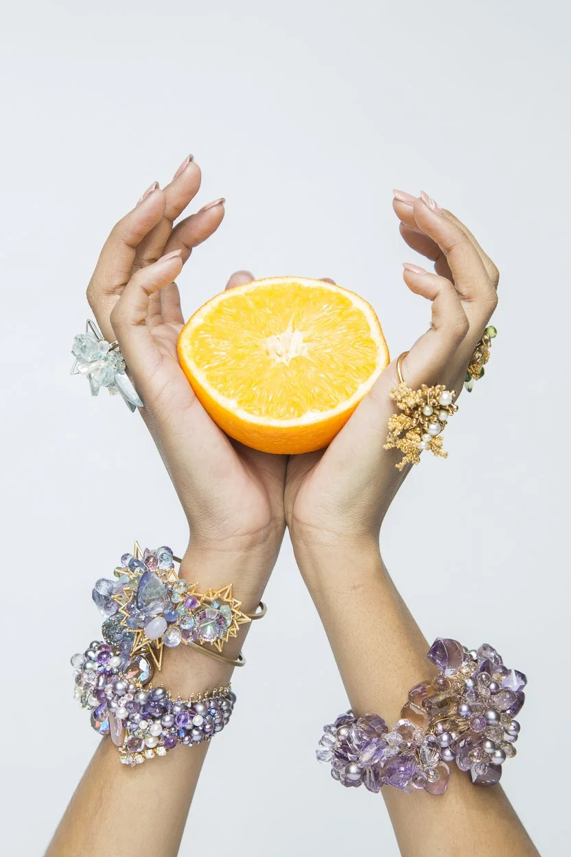 model hand holding a lemon wearing multiple statement bracelets and rings