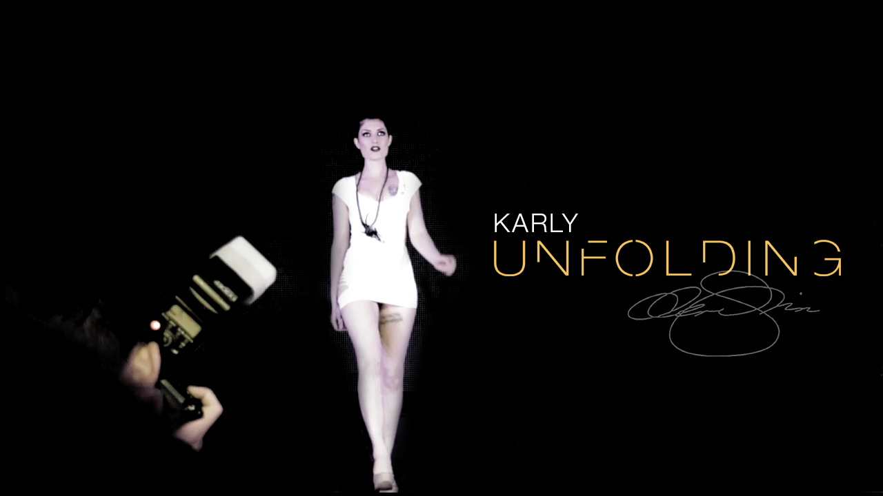 Runway model in a short white dress and long pendant necklace walks toward the camera beneath the title “Karly Unfolding.”