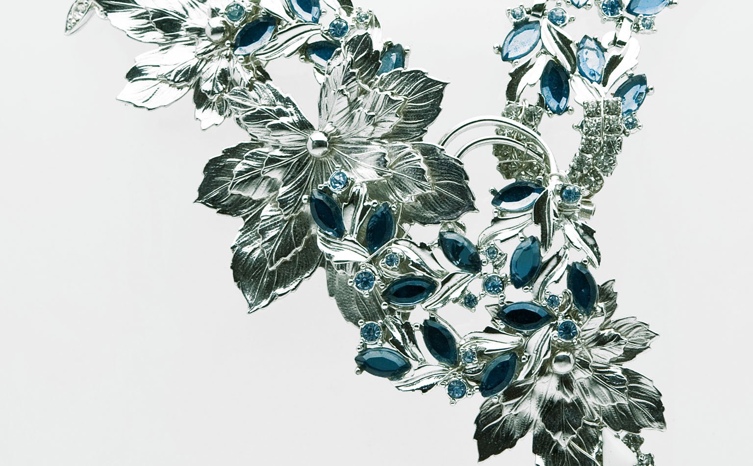 Silver-tone leaves and blue crystal along the curve of a necklace 