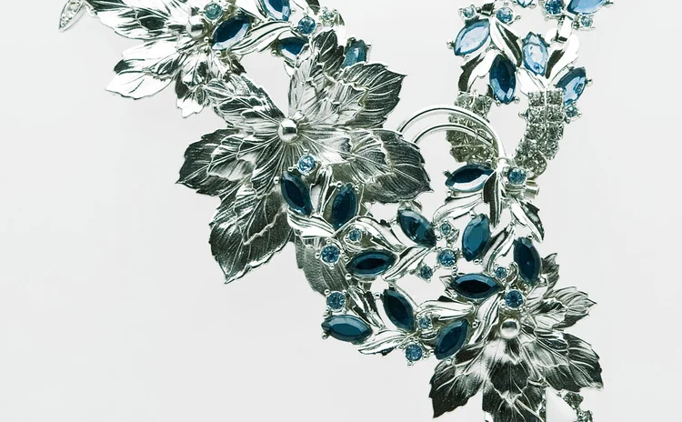 Silver-tone leaves and blue crystal along the curve of a necklace