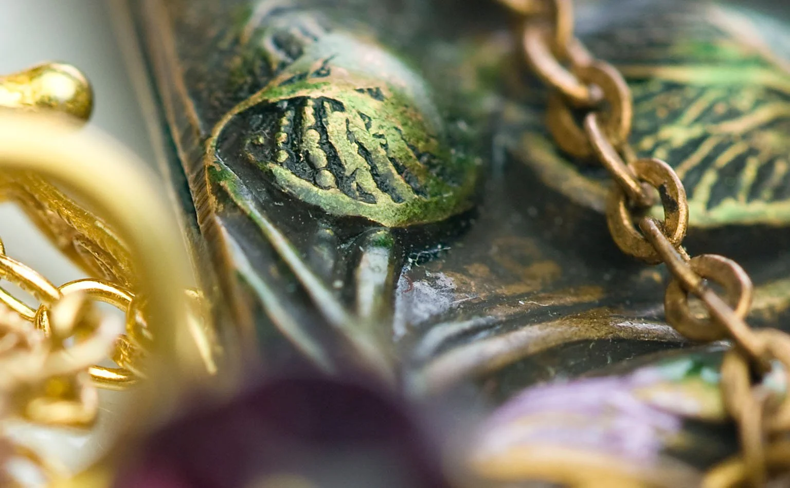 Detail of gold-tone chain against green enamel leaves