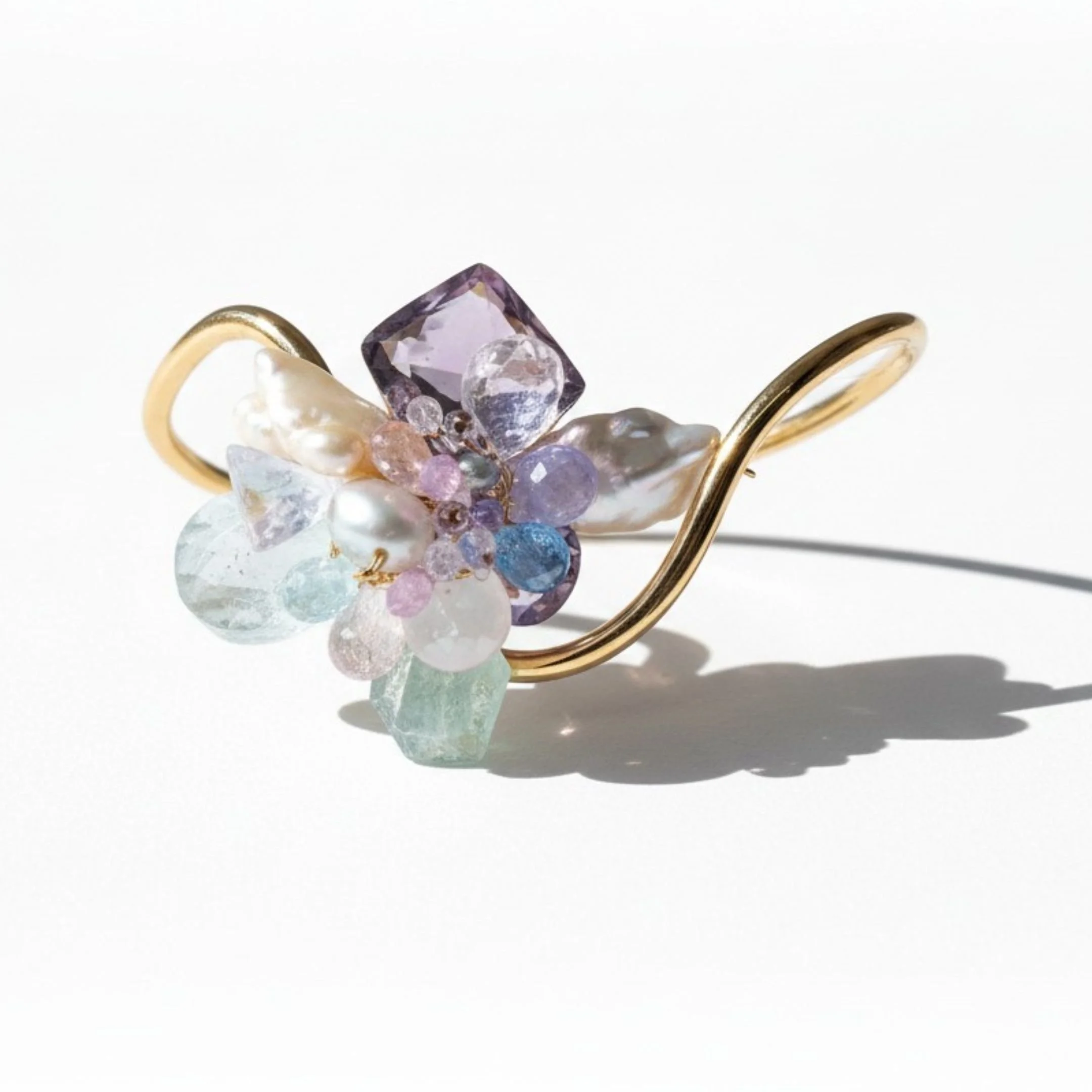 Gold bangle featuring a faceted pink gemstone with pastel blue, pink, and clear crystal clusters, shown with editorial text.
