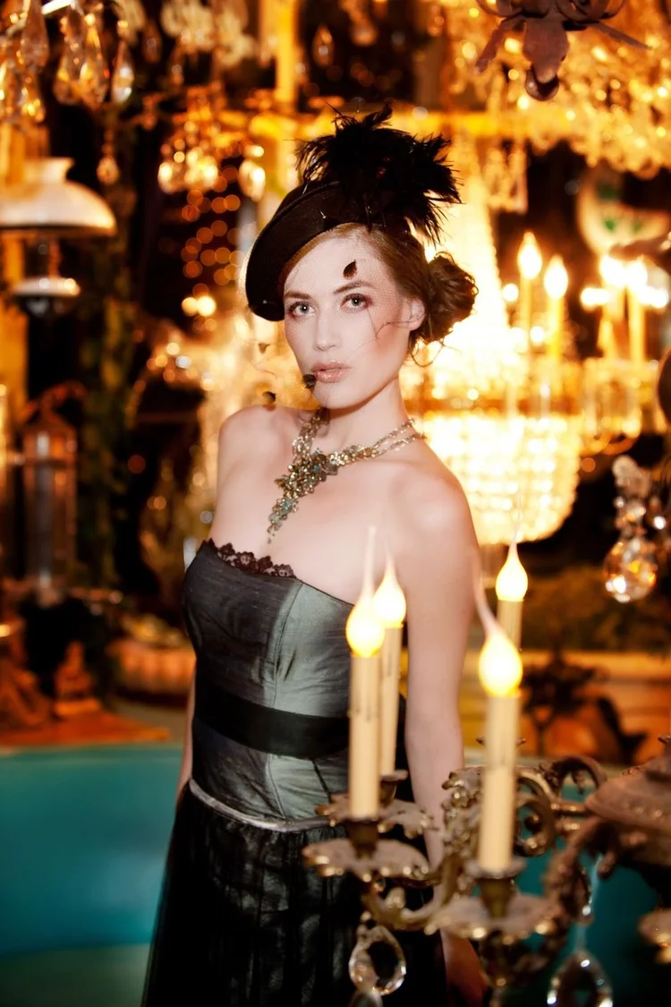 A model in a teal and black dress beside candle chandeliers