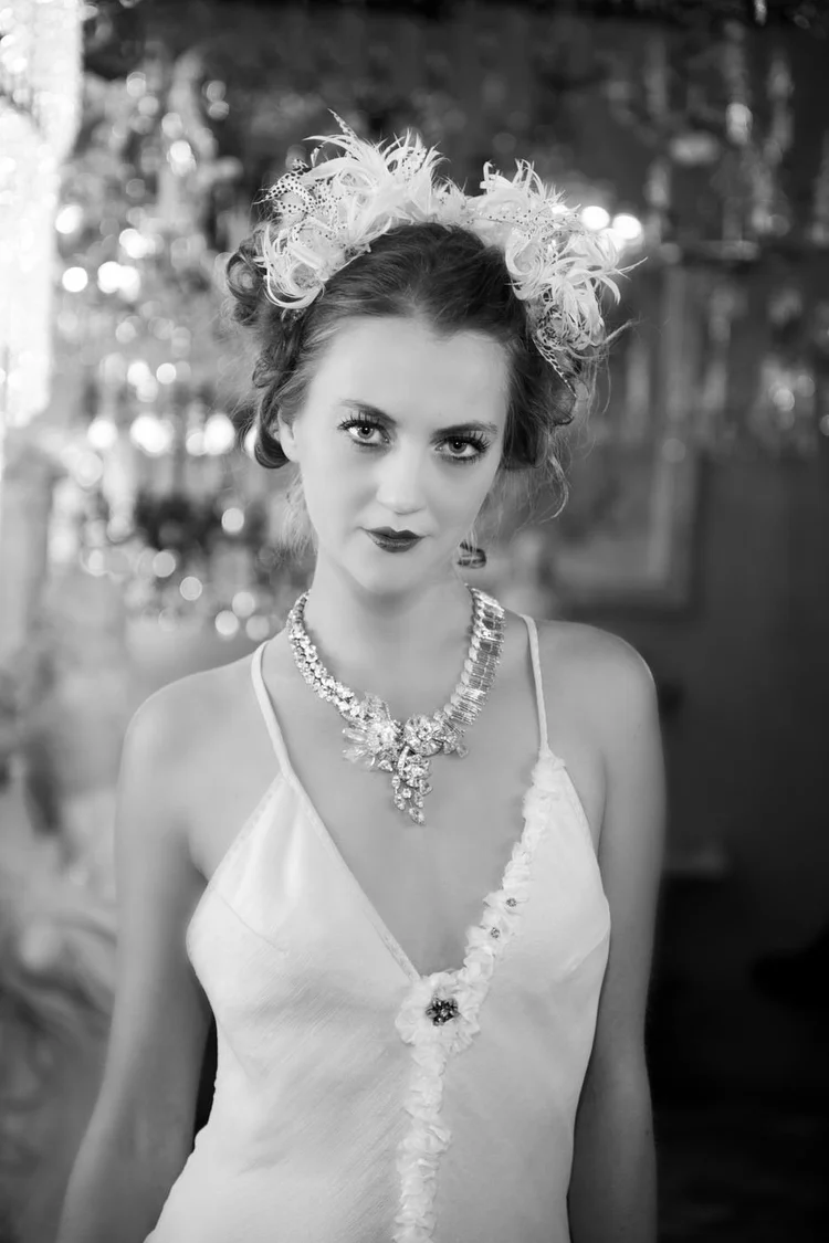 A red-lipped model with a white feather headpiece and a rhinestone statement necklace