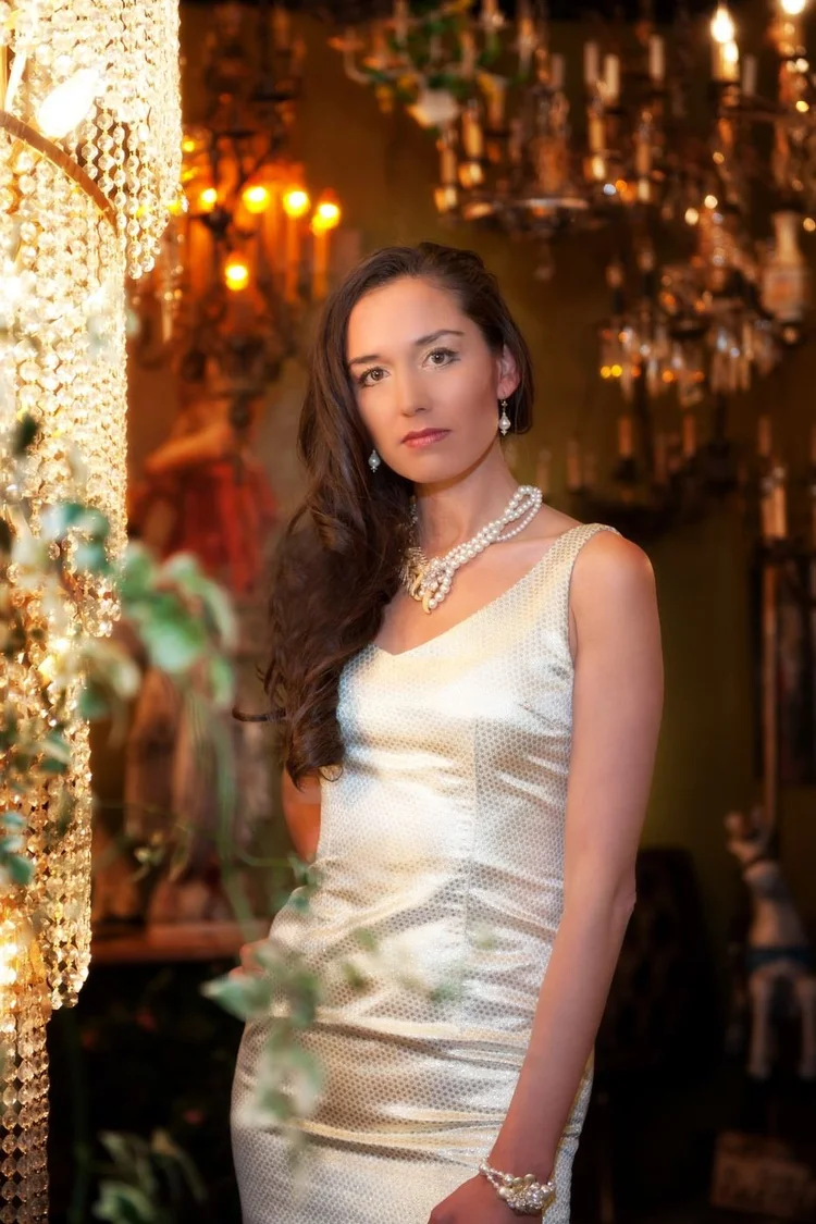 A model in a white satin dress beside a chandelier