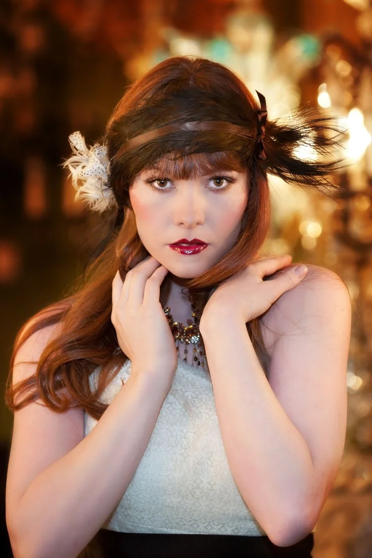 A model with a feather headband, hands at her neck, Andrea Li necklace