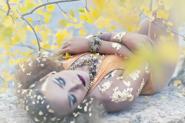 The model in gold leaf reclining among aspen leaves, landscape view