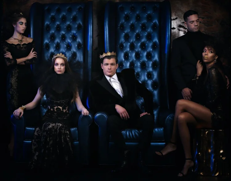 The Royals opener image: five crowned models on a blue tufted throne set, one wearing an Andrea Li necklace