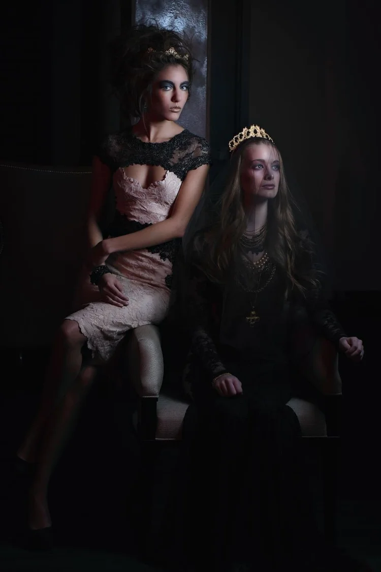 Two crowned models seated together in shadow