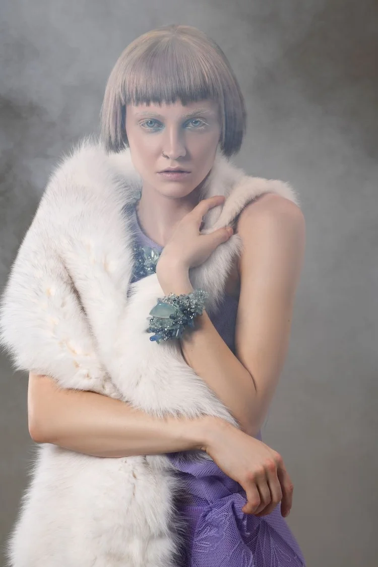 A model in a white fur stole and sequin dress with an Andrea Li green cluster cuff