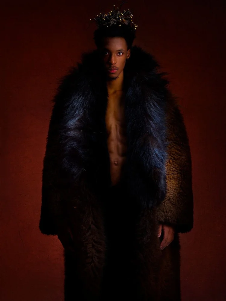 A man in a long dark fur coat with an Andrea Li gold spiked headpiece
