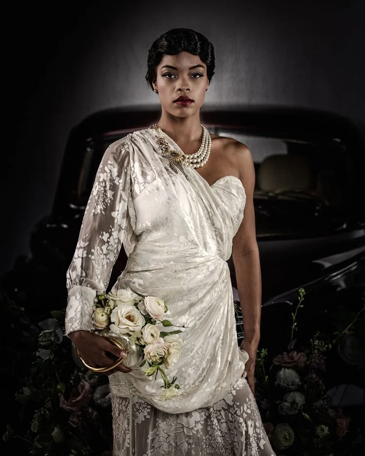 A model in an ivory lace one-shoulder gown with a bouquet
