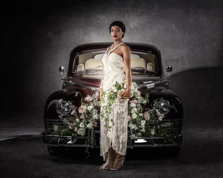 A model in a lace gown before the vintage car, pearls and an Andrea Li necklace