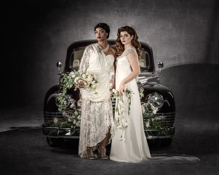 Two brides in ivory gowns together before the vintage car