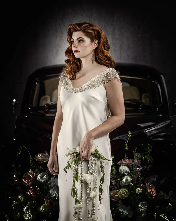 A red-haired bride in a beaded satin gown with a trailing bouquet
