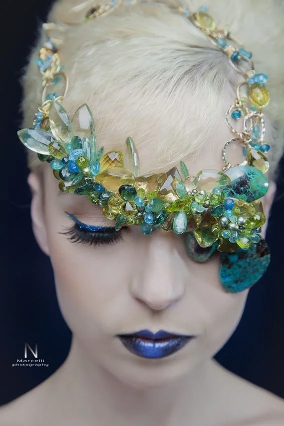 A platinum-haired model wearing an Andrea Li blue and green crystal cluster piece across one eye like a mask