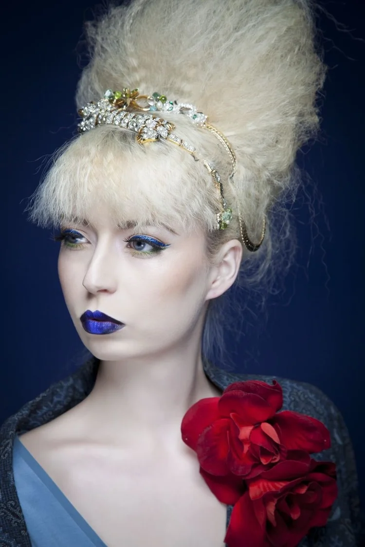 Close portrait: a platinum beehive with a jeweled Andrea Li headband, blue lips and a red flower