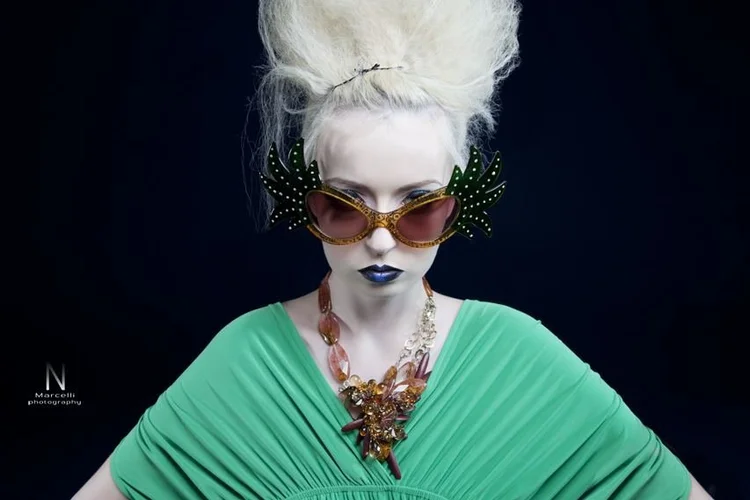 A platinum beehive, green drape, novelty glasses and an Andrea Li cluster necklace