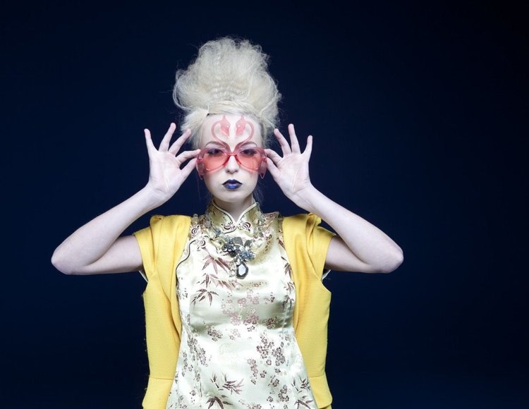 A model in a yellow cardigan and floral top, hands framing her face, Andrea Li necklace, landscape view