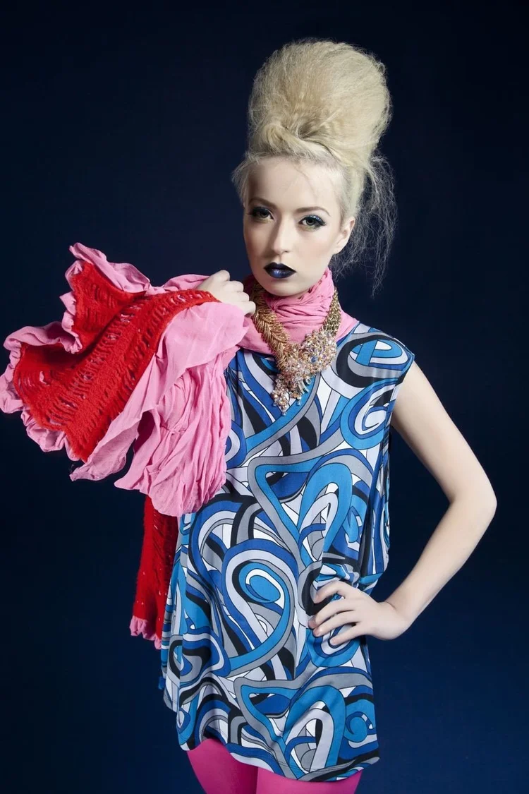 A model in a blue swirl print top with a red and pink ruffle and an Andrea Li necklace