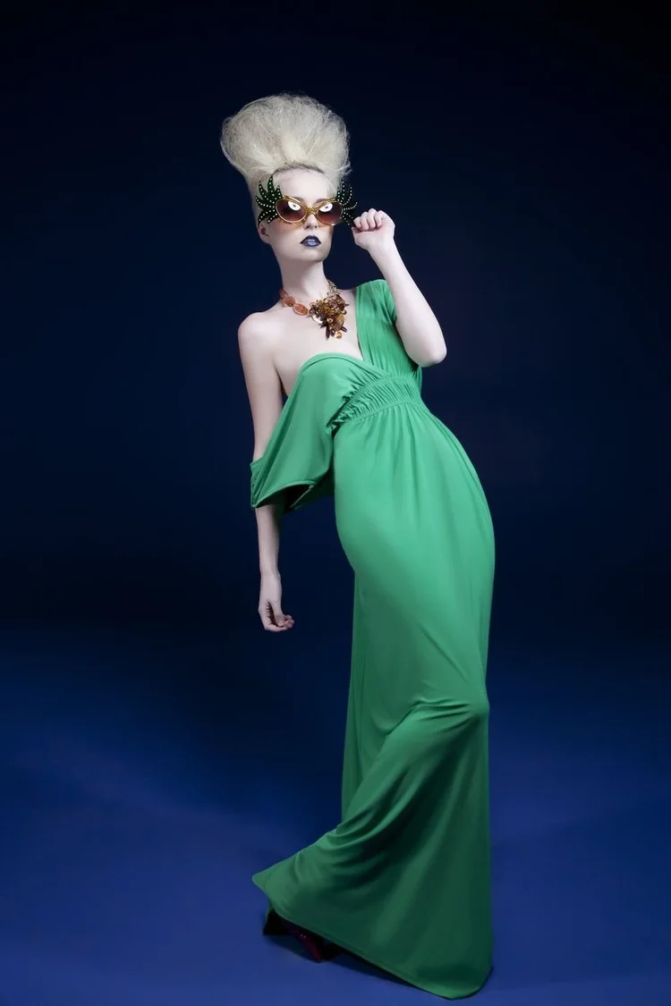 Full length in a long green gown with novelty glasses and a platinum beehive